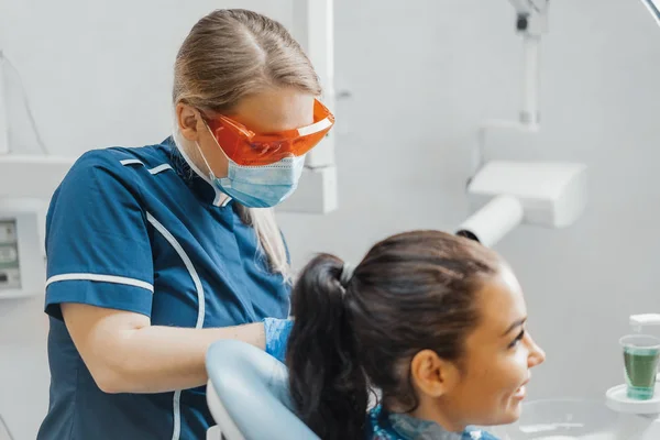 Nahaufnahme einer Zahnärztin, die einer lächelnden Kundin eine Plastikschürze aufsetzt. — Stockfoto