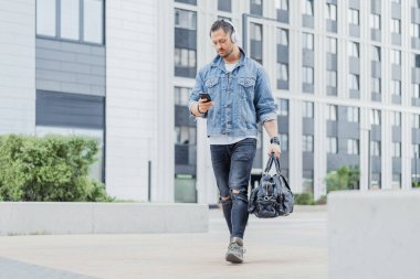 Kulaklık cep telefonunu gidiş sırasında bakarak adamın uzak planı.