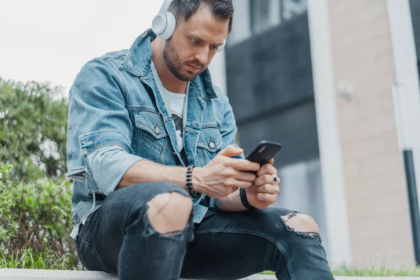 Primer plano del joven en auriculares y mirando el teléfono móvil . — Foto de Stock