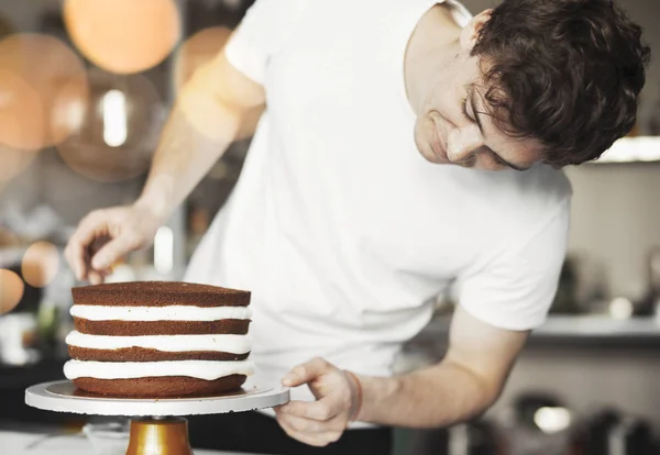 Close up of young man decorating chocolate cake by butter cream. — Stock Photo, Image