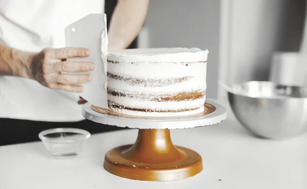 Close up of cook smearing butter cream on dark chocolate cake. — Stock Photo, Image