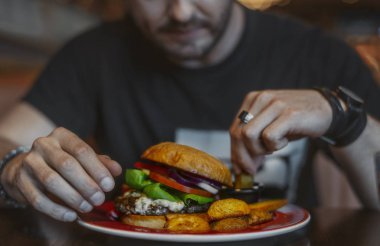 Genç çekici adam yeme hamburger ve patates kızartması Café.