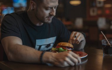 Genç çekici adam yeme hamburger ve patates kızartması kafe yakın çekim.