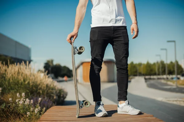 Primer plano del joven sosteniendo longboard o monopatín en el parque . —  Fotos de Stock