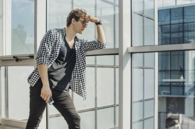 Genç adam büyük windows metro istasyonu yanında ayakta uzak planı. Adam siyah tişört içinde odak ve ön plan, metro istasyonu arka plan üzerinde.