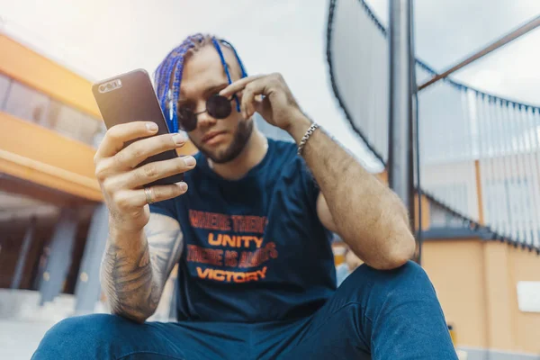 Joven hombre atractivo con rastas azules mirando a la pantalla del teléfono móvil . —  Fotos de Stock