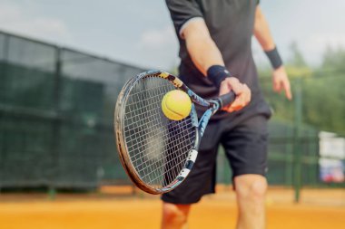 Tenis kortunda tenis oynayan ve raketle topa vuran çekici bir genç. Oyuncu maç yaparken raketle topa vuruyor.