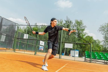 Tenis kortu tenis oynamak ve topu raket ile yenerek genç çekici adam uzak planı. Düzle grev ile topu atan oyuncu.