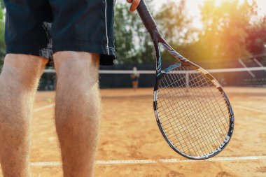 Tenis kortunda top beklerken Man Holding Raket 'i kapatın. Erkek odaklanıyor ve ön planda, tenis ağı arka planda ve bulanık.