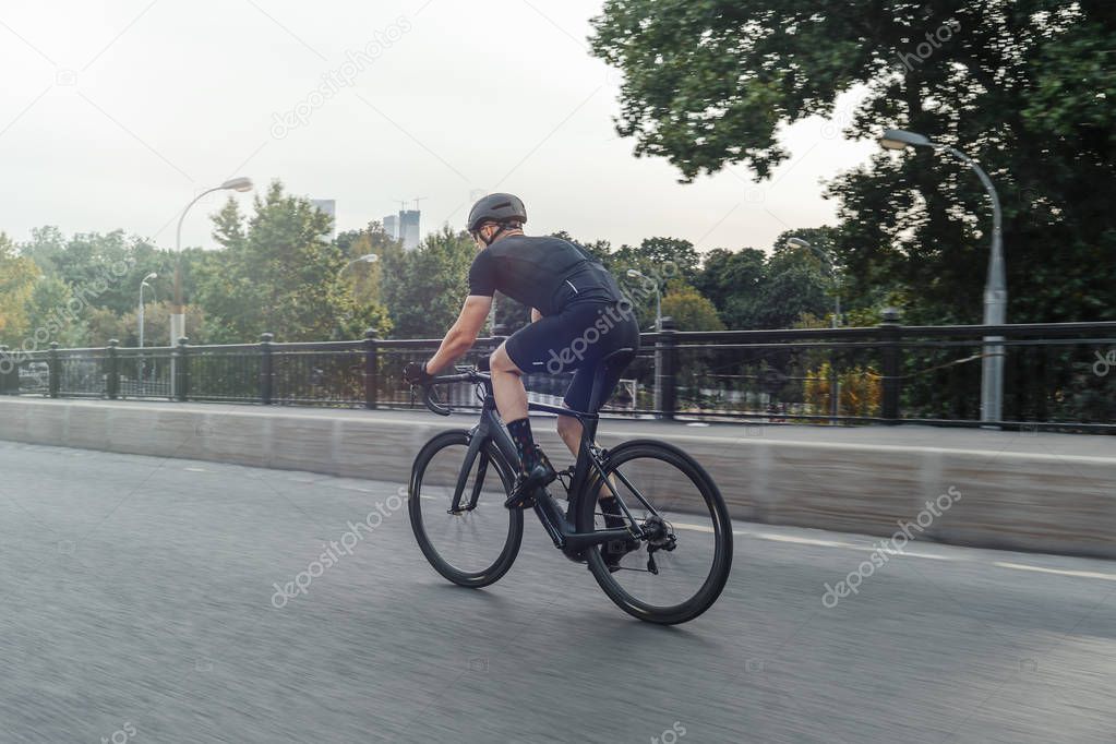 Athletic sportsman riding professional bike in race on a road on concrete bridge. Cyclist on professional bicycle training day. Concept of active lifestyle and outdoor hobby.