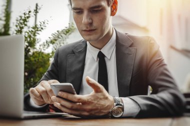 İşadamı laptop yanında oturan, cep telefonu tutan ve ekrana bakarak sokak kafe yakın çekim. Önden görünüm.