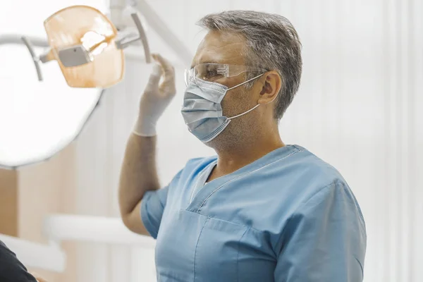 Dentista de uniforme azul sentado ao lado de equipamentos odontológicos . — Fotografia de Stock