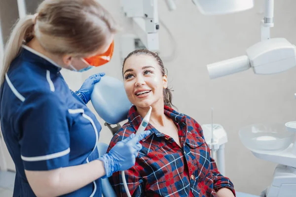 Close up de cliente sorrindo para dentista segurando instrumentos dentários . — Fotografia de Stock