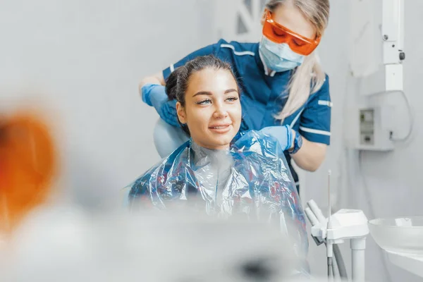 Close up of woman dentist putting on plastic apron on smiling woman client.