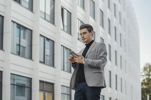 Plano distante do jovem empresário falando por telefone celular ao lado do arranha-céu . — Fotografia de Stock