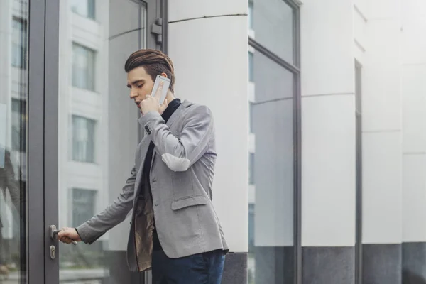 Plano à distância do jovem homem de negócios falando por telefone celular e abrindo uma porta . — Fotografia de Stock