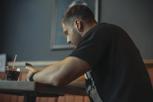 Joven atractivo hombre pensativo mirando la pantalla del teléfono móvil y beber refrescos . — Foto de Stock