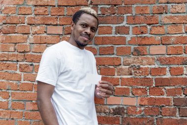 Esmer adam tuğla zemin üzerine beyaz T-shirt gösteren iş kartı.