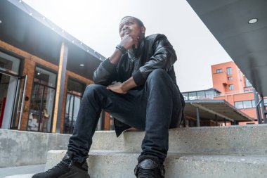 Modern tuğla bina somut adımlar üzerinde oturan dalgın adam koyu tenli.