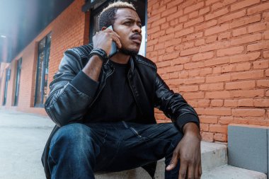 Cep telefonuyla konuşurken ve kırmızı tuğla modern bina somut adımlar üzerinde oturan esmer dalgın rahatsız insanın yakın çekim.