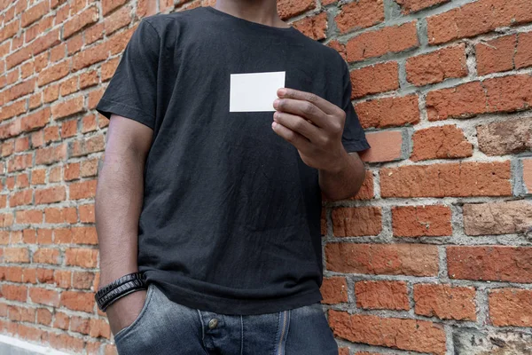 Esmer adam boş kartvizit tuğla arka plan üzerinde gösterilen T-shirt.