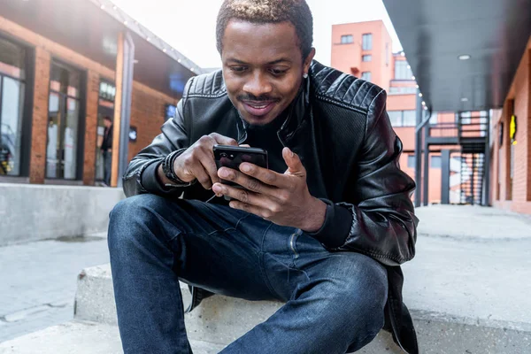 Primer plano del hombre sonriente de piel oscura mirando la pantalla del teléfono móvil . — Foto de Stock