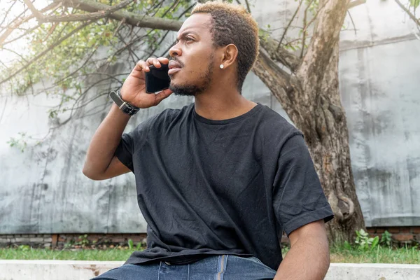 Primer plano del pensativo hombre de piel oscura en camiseta negra hablando por teléfono móvil . —  Fotos de Stock