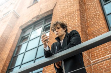 Merdiven üzerinde duran ve cep telefonu ekranına bakarak çekici dalgın adam.