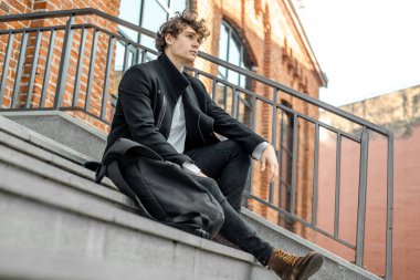 Modern kırmızı tuğla bina somut adımlar üzerinde oturan dalgın adam.