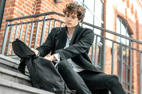 Bina ve sırt çantasında karıştırmak modern kırmızı somut adımlar üzerinde oturan genç çekici dalgın adam tuğla.