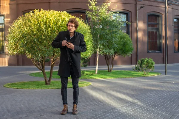 Genç adam kırmızı tuğla binalar ve yeşil ağaçlar geçerken uzak planı.