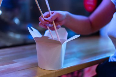 Kadar yakın Asya gıda beyaz karton kutu ve yemek çubukları tutmak el.