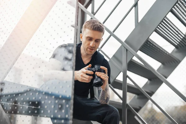 Hombre atractivo sentado en la escalera y la comprobación de fotos en la cámara . — Foto de Stock