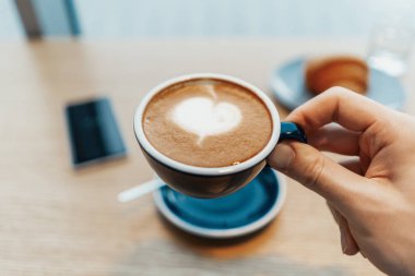 Kahve holding adam eller. Kruvasan ve cep telefonu arka plan üzerinde vardır.