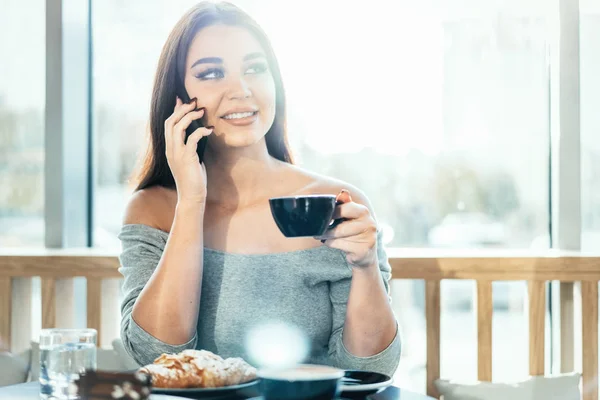 Hermosa mujer sosteniendo la taza azul de café y hablando por teléfono móvil . — Foto de Stock