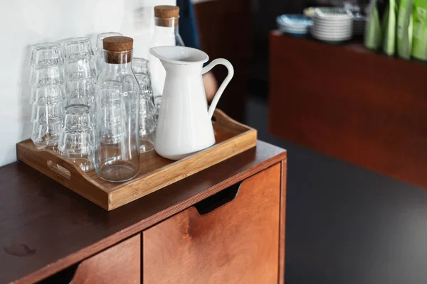 Verres transparents et pot en métal blanc sur placard en bois dans le café . — Photo