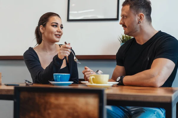 Pareja joven sentada en la cafetería en la cita, tomando café y comiendo postre . — Foto de Stock