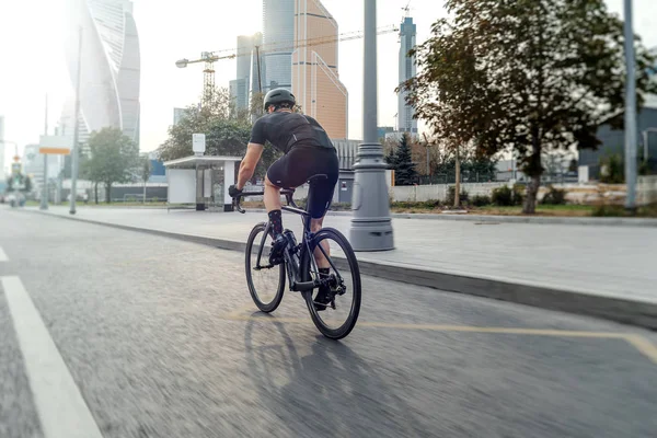 Atlético deportista montar en bicicleta profesional junto a edificios modernos en una carretera . —  Fotos de Stock