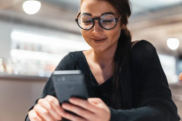 Ung vacker kvinna som håller mobiltelefon i händer i väntan på hennes måltid. — Stockfoto