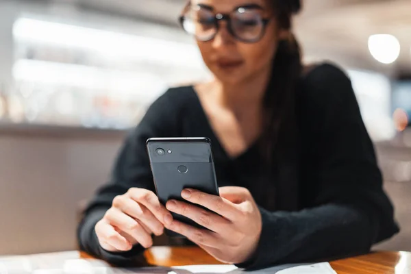 Ung vacker kvinna som håller mobiltelefon i händer i väntan på hennes måltid. — Stockfoto