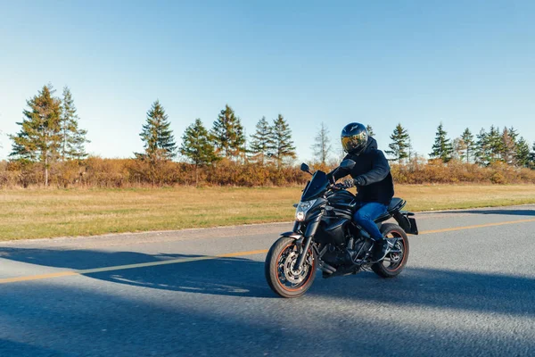 Sürücü güzel sonbahar ormandaki boş yolda motosiklet Binme. Uzak planı, yan görünüm.