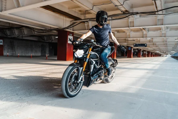 El plan lejano del motorista en el casco que monta la motocicleta en el estacionamiento. Fondo urbano . —  Fotos de Stock