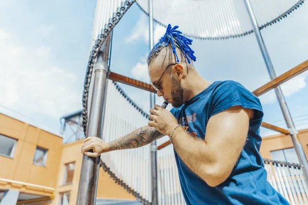 Retrato del joven vapeo con rastas en el fondo del objeto de arte. Concepto de vapor. Vaping e-Cigarette —  Fotos de Stock