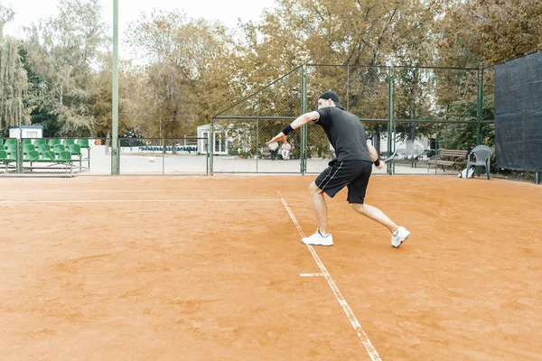 Plan distante de hombre jugando al tenis en la cancha y golpeando la pelota con una raqueta . — Foto de Stock
