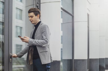 Hareket eden telefon tutarak ve bir kapı açmaya genç iş adamı uzak planı.