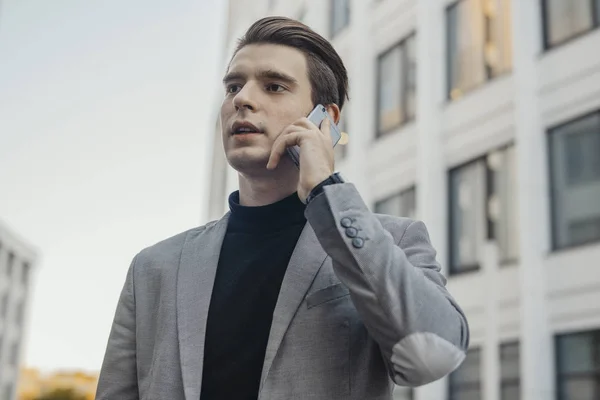 Zbliżenie na młody biznesmen rozmawia przez telefon komórkowy, obok centrum biznesowego. — Zdjęcie stockowe