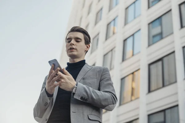 Zbliżenie na młody biznesmen rozmawia przez telefon komórkowy, obok centrum biznesowego. — Zdjęcie stockowe