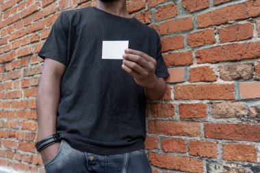 Esmer adam boş kartvizit tuğla arka plan üzerinde gösterilen T-shirt.