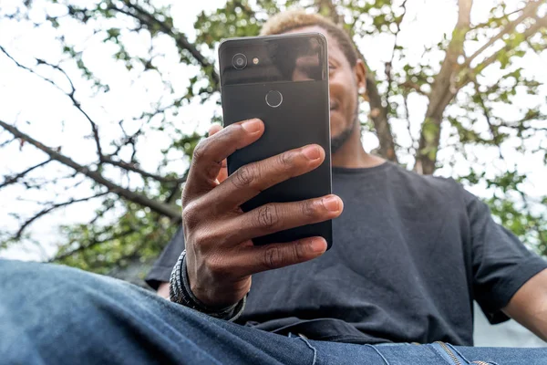 Pensativo hombre de piel oscura en camiseta negra mirando a la pantalla del teléfono móvil . — Foto de Stock