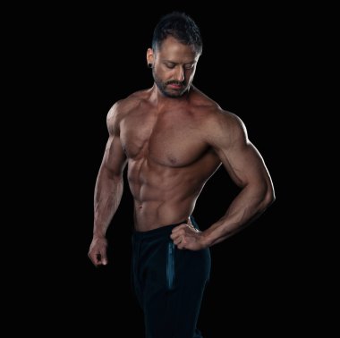 Acımasız güçlü vücut geliştirmeci atletik erkek siyah arka plan üzerine poz.
